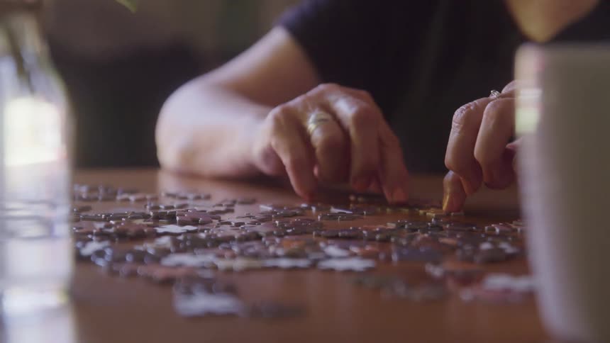 Hands assemble puzzle pieces on a wooden table