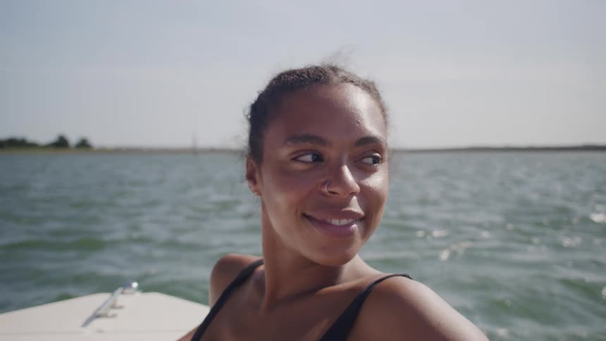Smiling woman in a black swimsuit enjoys a boat ride on the sea