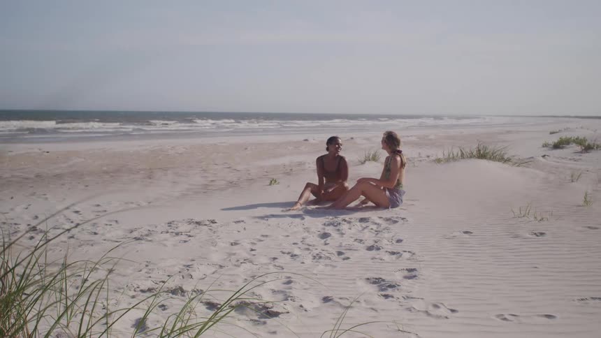 Two people talk while sitting on the sand of a deserted beach
