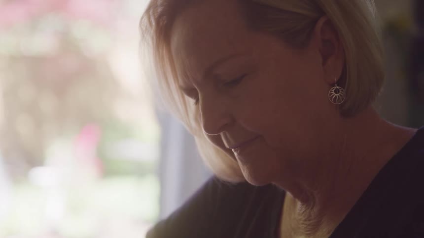 Woman with short blonde hair wears a silver earring while looking down thoughtfully