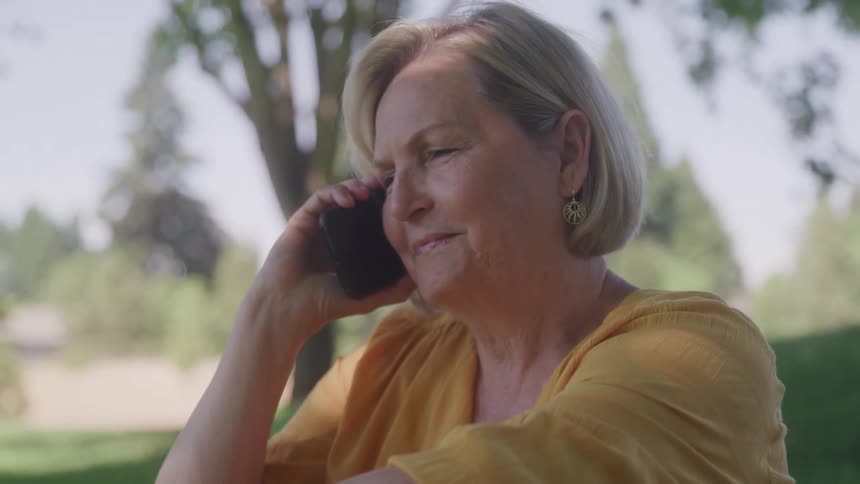 A woman smiles while on the phone outdoors