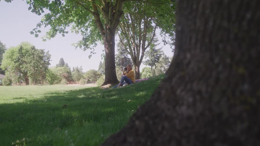 Woman sitting in the shade of a tree in a grassy park on a sunny day