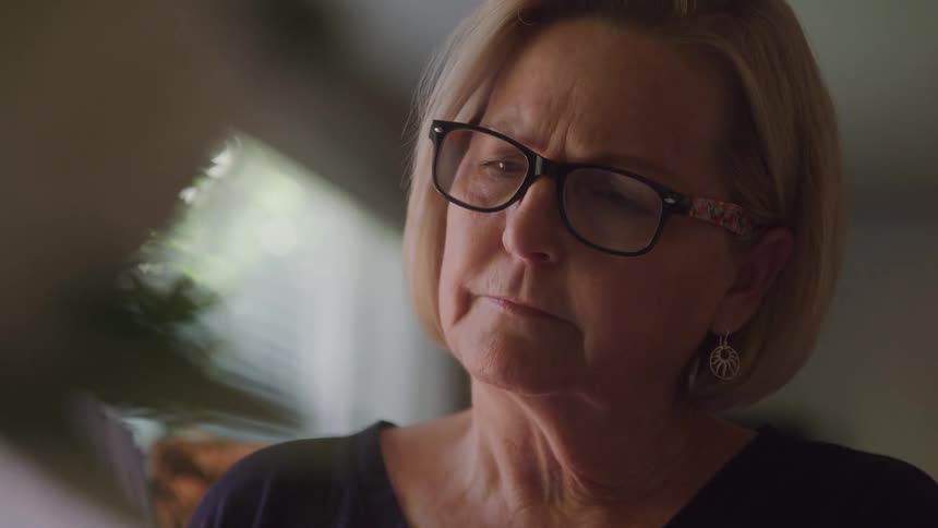 Woman with glasses smiles slightly while looking at something out of focus