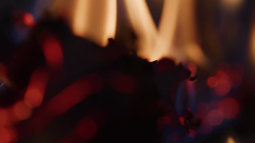 Flames flicker and embers glow in an intense closeup of a burning object