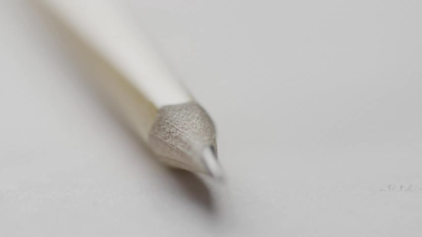 A sharpened pencil lies on a white surface its pointed tip in crisp focus against a blurred background