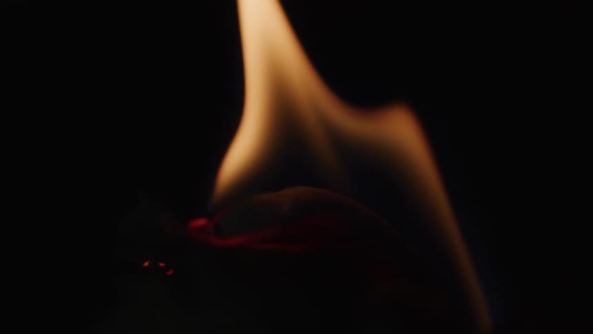 Orange flame lights up the dark while consuming a wick