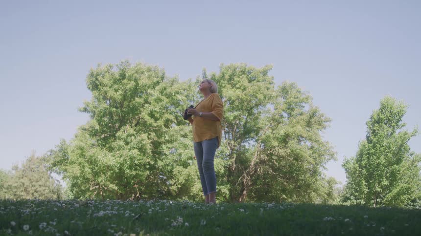 Woman in a yellow blouse looks at the sky in a treefilled park