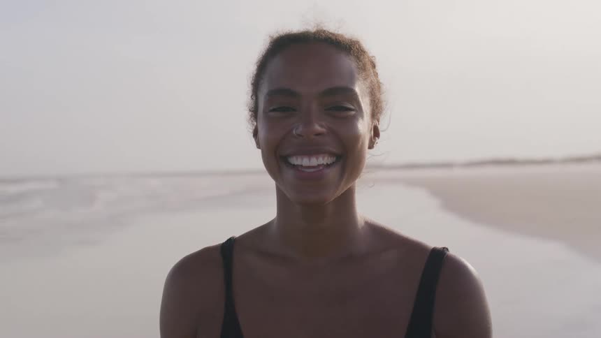 Woman in a black swimsuit smiles at the beach with the sea in the background