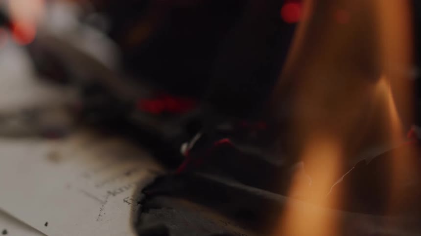 Charred blackened paper curls and burns as orange flames consume the page