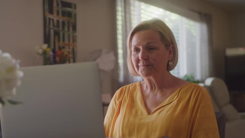 Woman in a yellow blouse smiles and waves during a video call