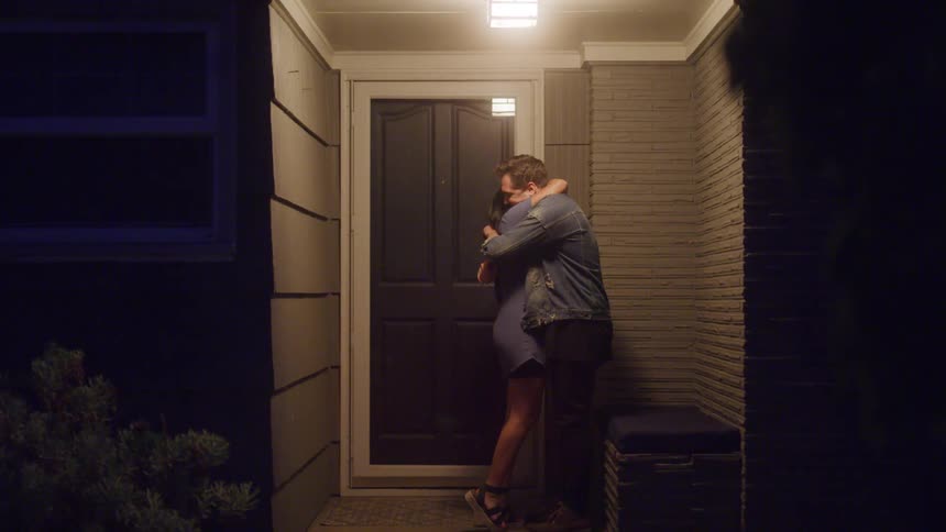 Couple kisses holding hands in front of a lit doorway at night
