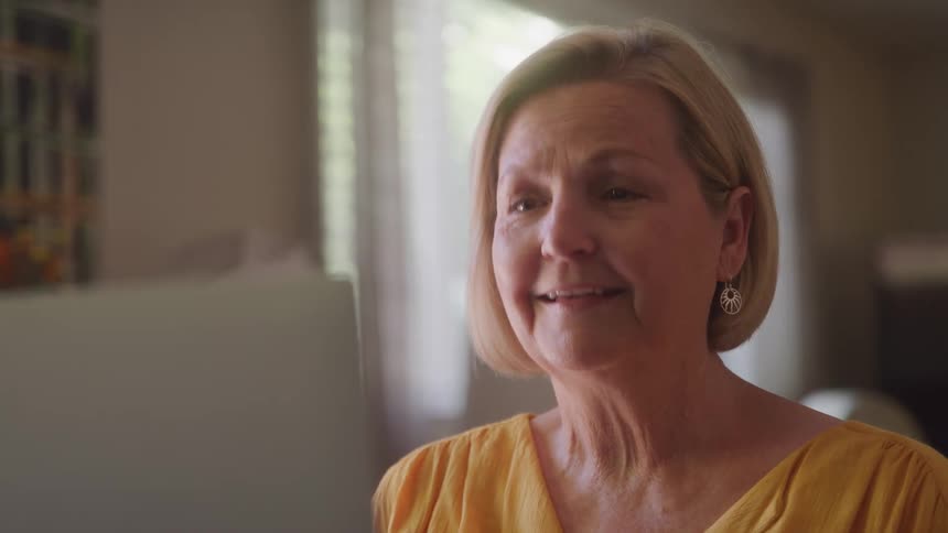 Woman in a yellow blouse smiles while looking at the computer screen