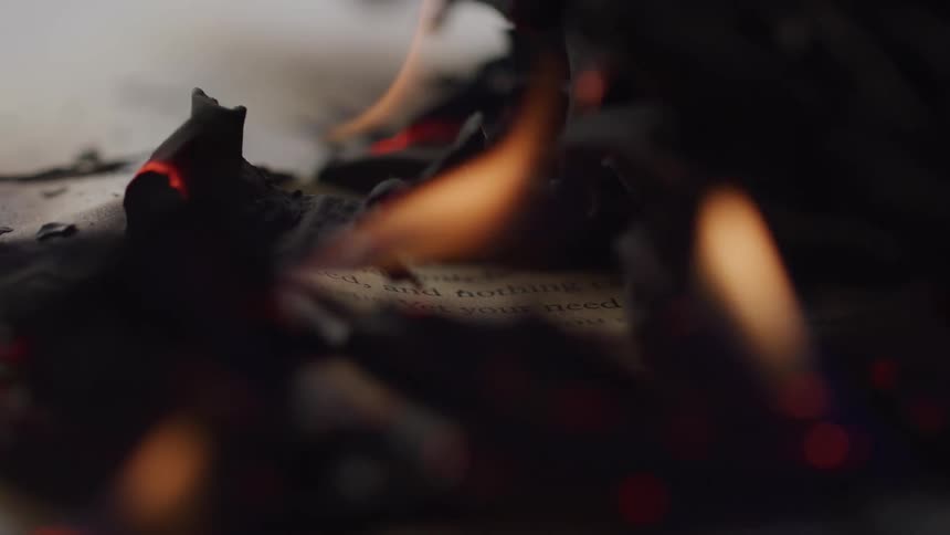 A piece of paper burns slowly as flames and glowing embers reveal partially visible text