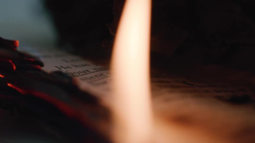 Focused flame illuminates printed words on a partially burned page