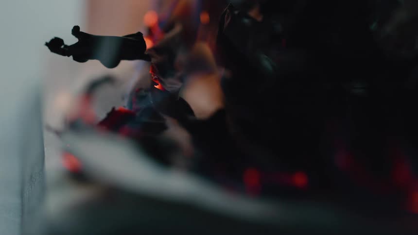 A closeup of burning paper reveals glowing embers and curling ash in vivid detail