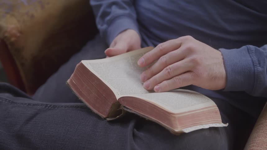 En person flips through a thick hardcover book resting on their lap