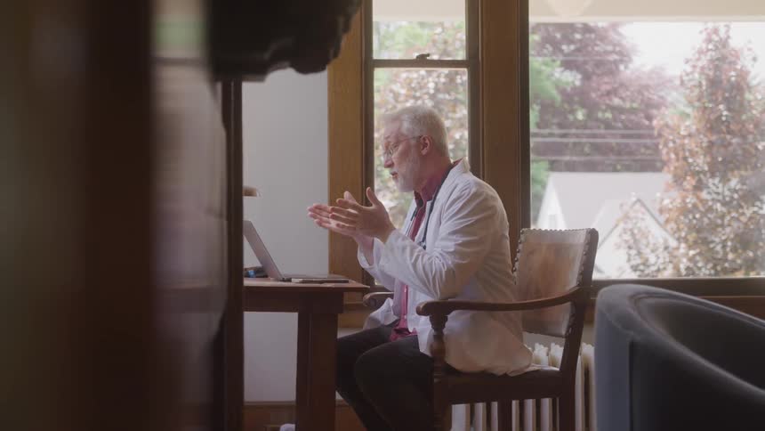 Doctor sitting in front of a laptop gestures during a video call