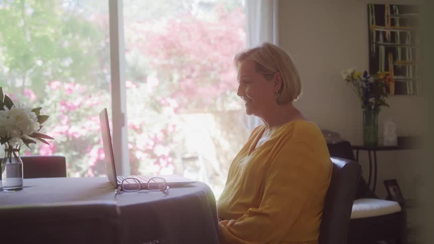 An older woman video chats on a laptop indoors