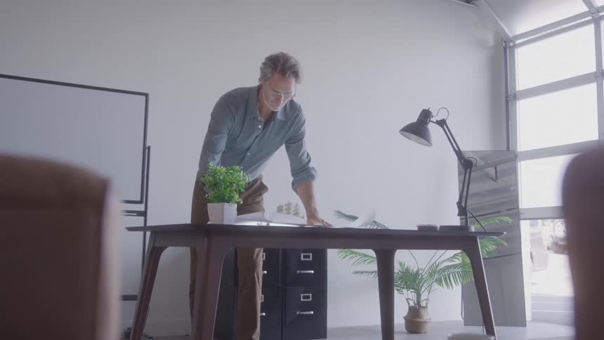 A man is leaning over a desk while working in a modern office space