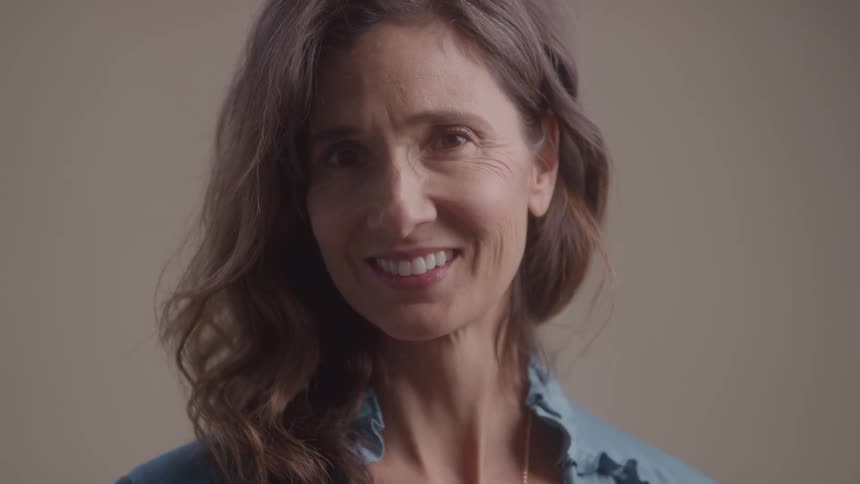 A woman in a blue top smiles warmly in a softly lit studio setting