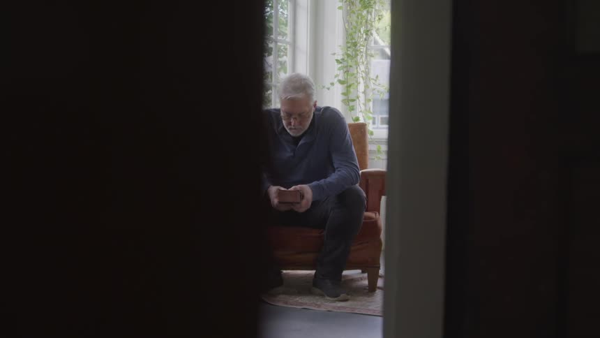 Man sits alone by a window holding a book and lost in thoughts