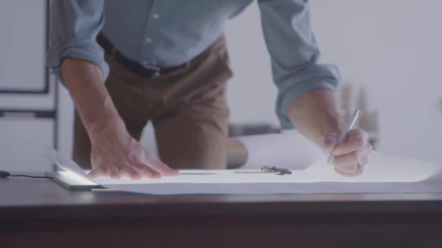 An architect works on a building document at a workbench indoors