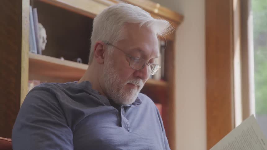 Man with glasses sitting in the living room reading a book