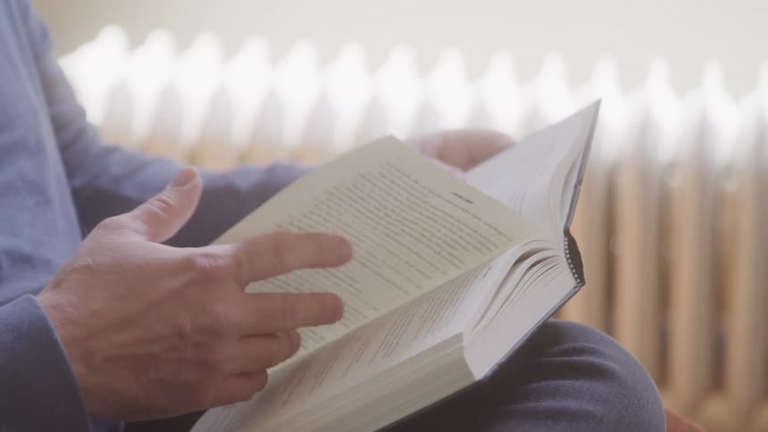 A person gently flips through a book while seated in soft natural light