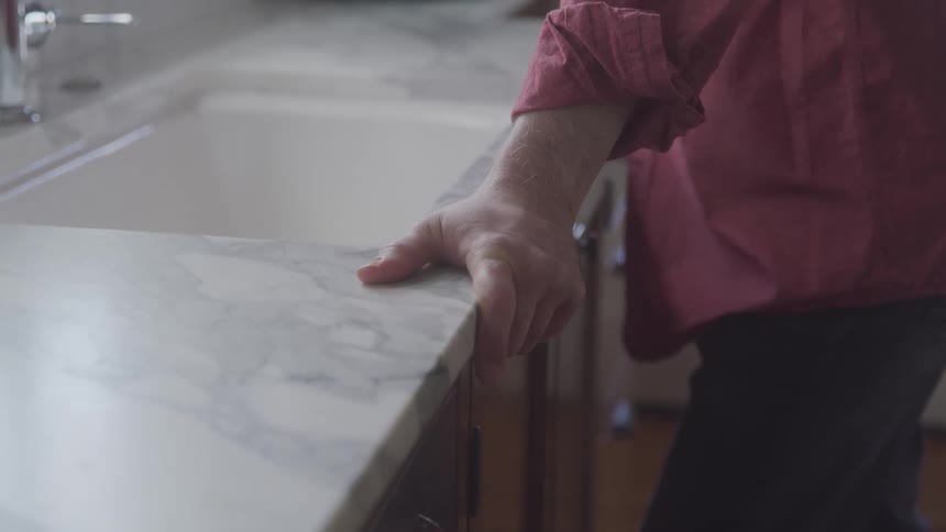 A mans hand grips a marble kitchen counter wearing a red shirt with rolledup sleeves