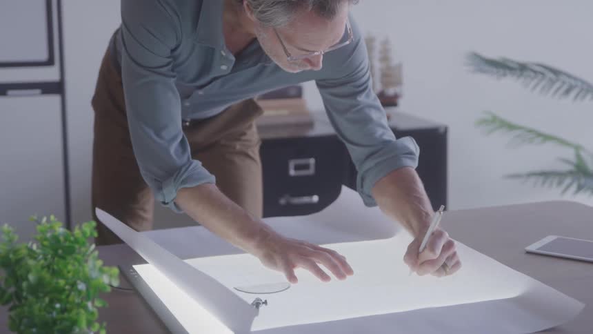 Man with glasses draws on a lighted table in a workspace