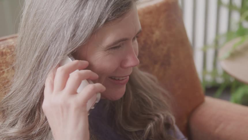 An elderly woman sitting in an armchair talking to someone on the phone and smiling