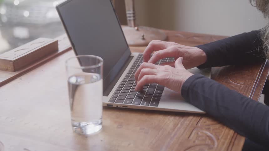 A person types on a laptop at a wooden desk indoors