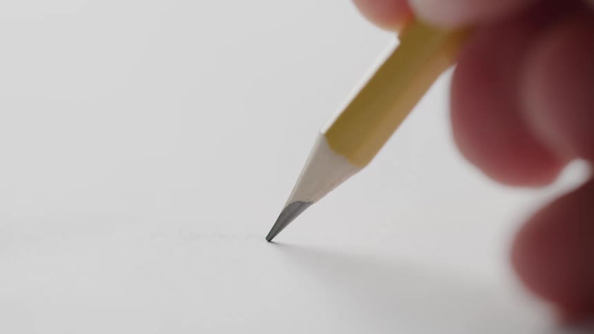 A hand gently presses a sharpened pencil to paper just beginning to draw or write