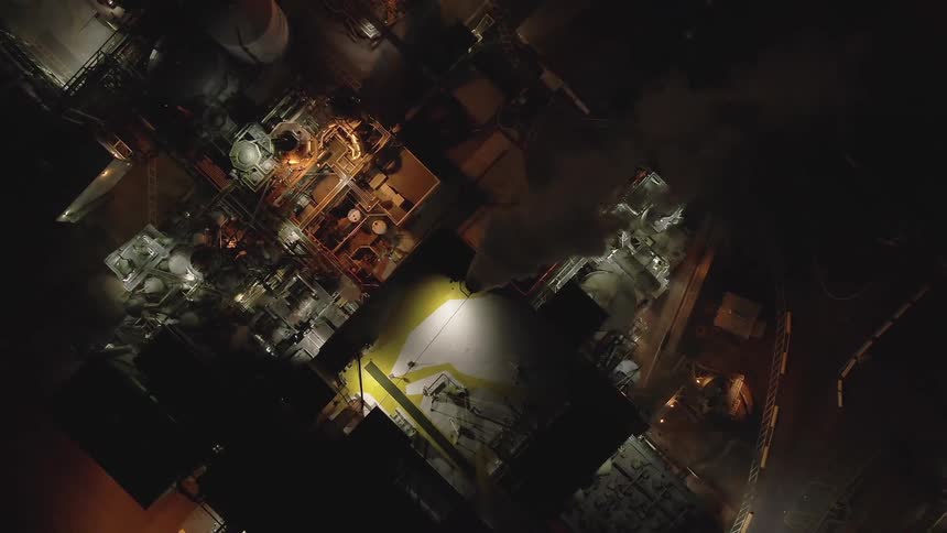 A complex industrial facility is illuminated from above in a dramatic nighttime aerial view