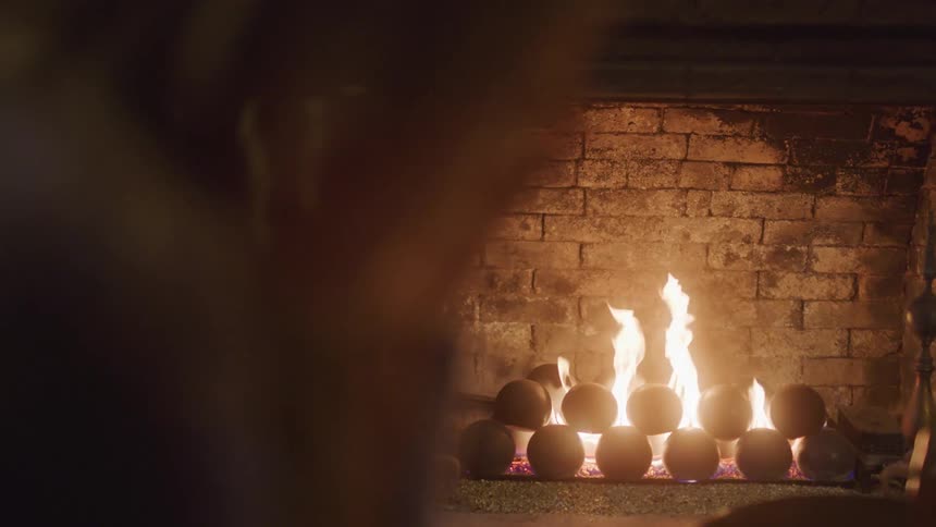 A warm fire burns in a brick fireplace with part of a persons head faintly visible in the foreground
