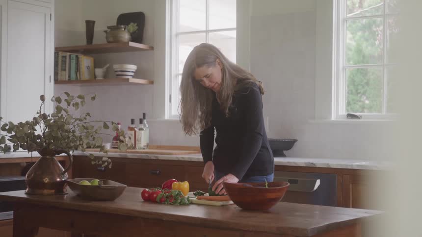 A woman is chopping vegetables alone in a cozy kitchen