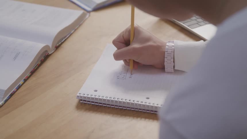 Person writes in a notebook with a pencil next to an open book
