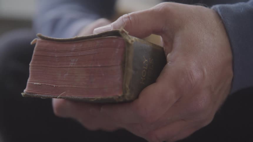 A pair of hands holds and flips through a very old worn book the book is thick with reddishbrown pages and a dark weathered cover
