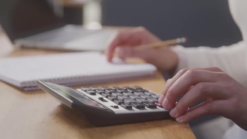 A closeup shot of a persons hands diligently using a calculator and holding a pencil over a notebook suggesting a focus on financial or mathematical work