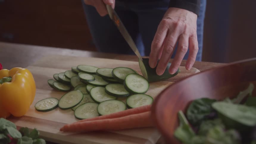 A woman slicing cucumber into thin pieces on a cutting board