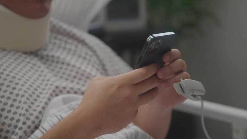 Hands of a patient person lying in a hospital bed typing on a smartphone