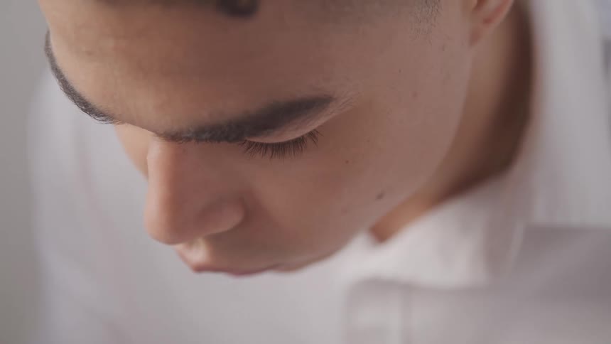 The video shows a closeup of a mans face with the camera focused on his eyes and nose as he looks down the video is a medium shot of a man in a white collared shirt with his face in focus looking down at something below him