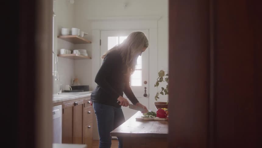A woman is cutting vegetables in a softly lit kitchen during the day