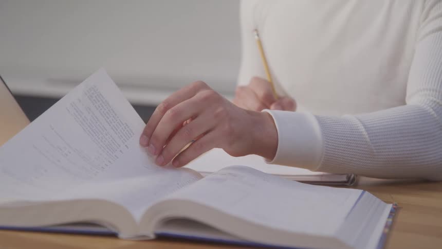 A closeup shot of a persons hands shows him studying holding a pencil with a white long sleeve shirt and a watch visible