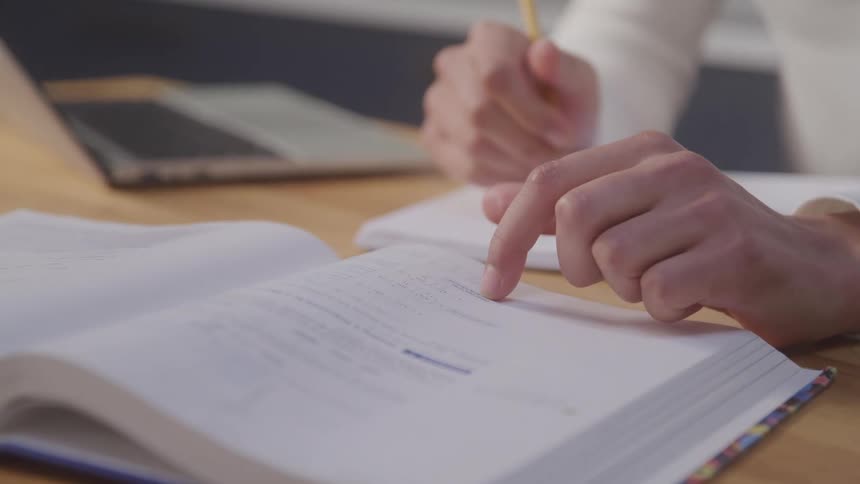 Person reads an open book and points to a passage with a finger while holding a pencil
