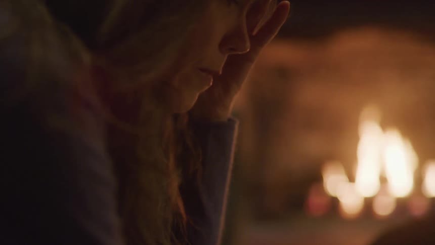 A woman sits beside a fireplace with flames burning in the fire