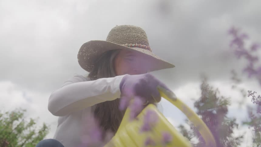 A woman is watering flowers in a garden with a cheerful expression