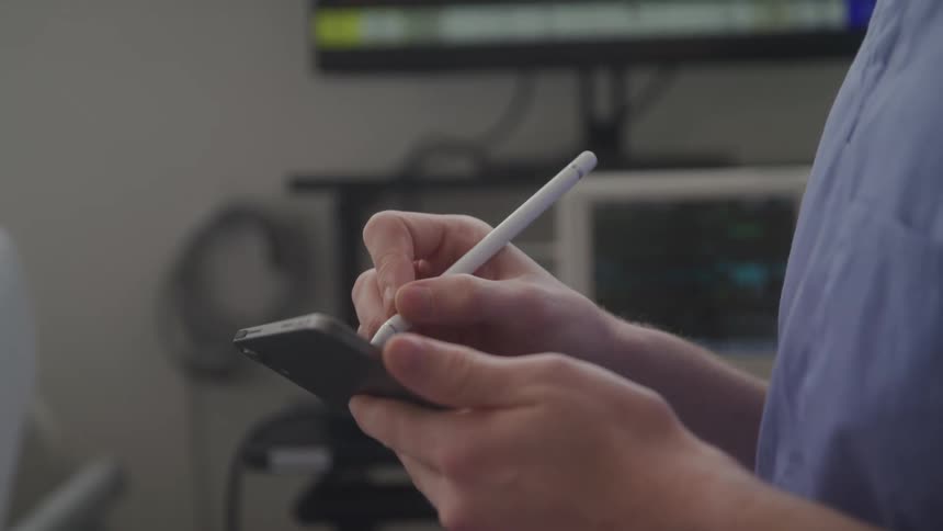 Person holding a tablet and using a digital pen in a setting with electronic equipment