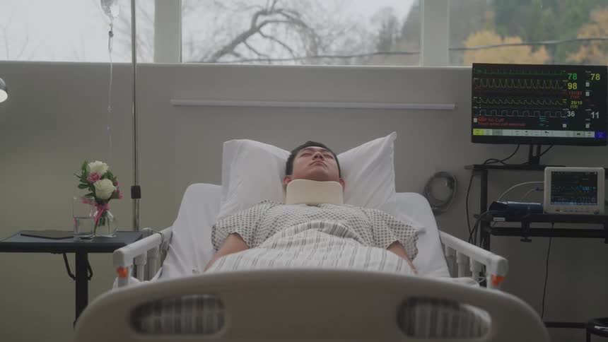 A patient lies in a hospital bed hooked up to medical monitors