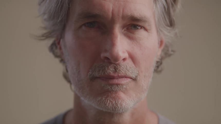 The video shows a closeup of a middleaged man with graying hair and a short beard he is seen turning his head to look directly at the camera with a neutral and somewhat introspective expression